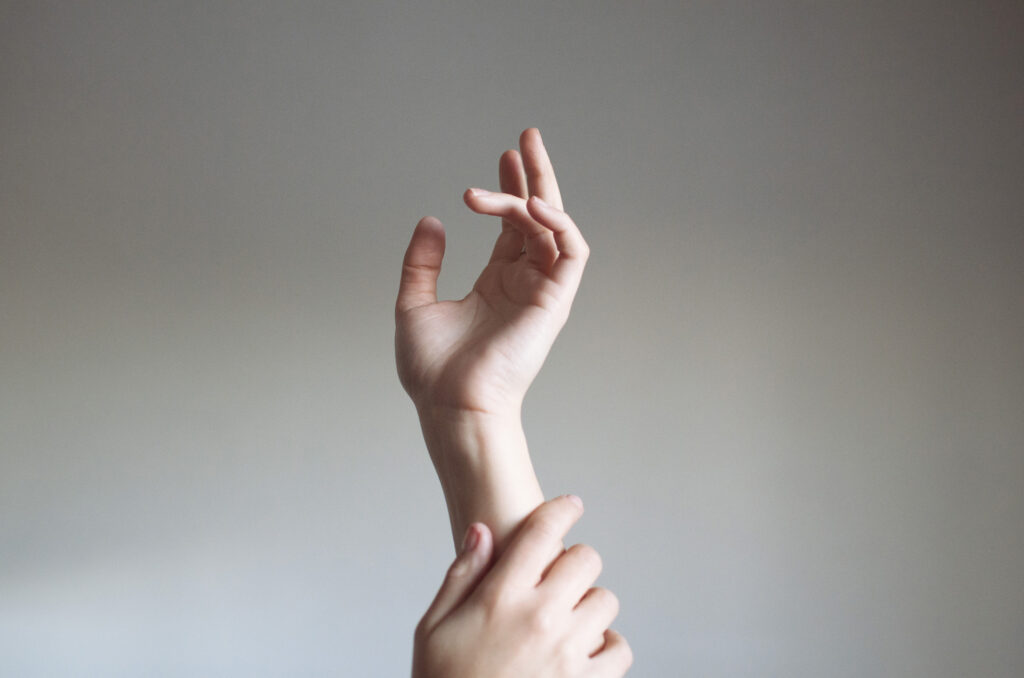 Laura Adriana photo showcases a delicate human hand reaching upwards with fingers gracefully curled set against a neutral background.